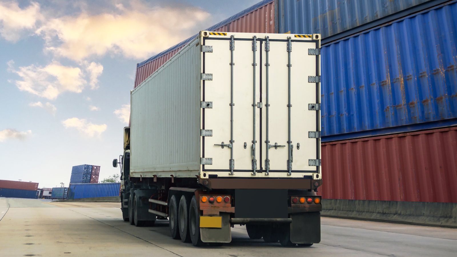 Container truck driving past stacked containers at a port terminal